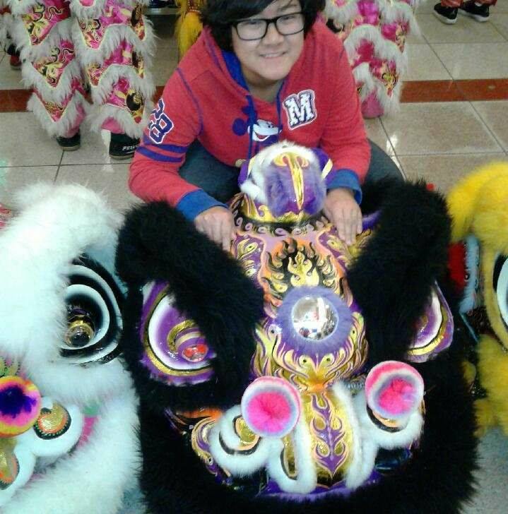 Vanessa is kneeling behind a dragon head. Vanessa is smiling and wearing a red and blue MickeyMouse Hoodie.